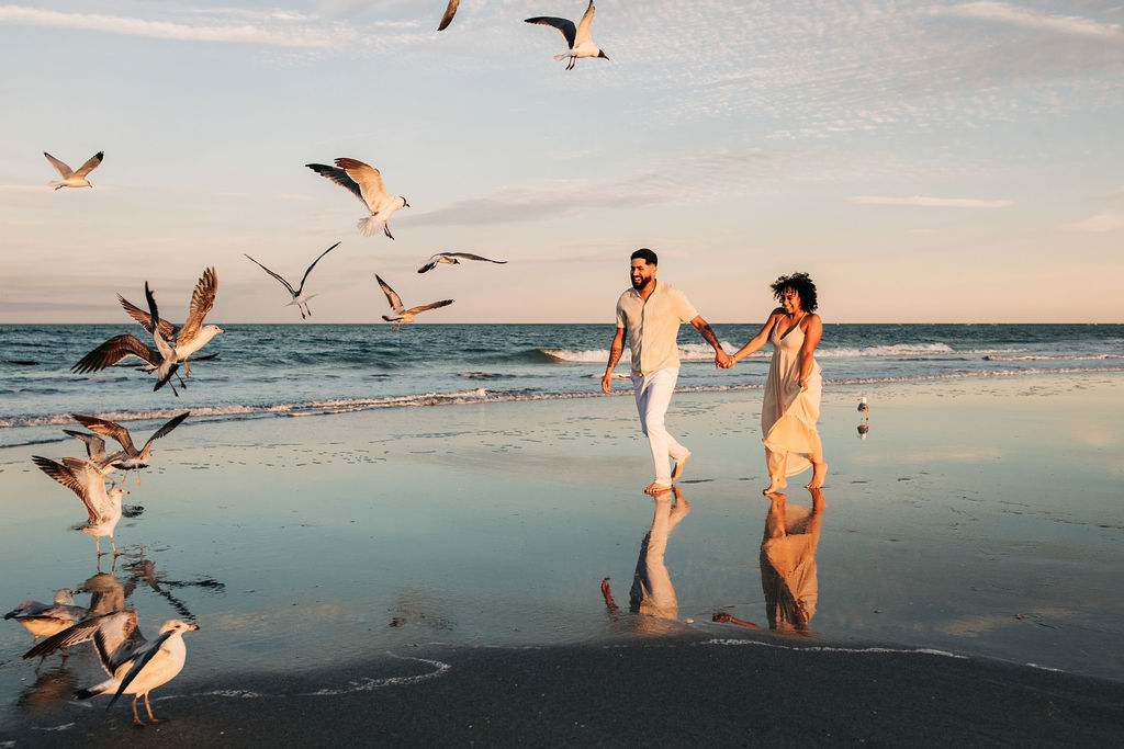 Couple running on the beach as seagulls fly away